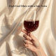 A hand holds a wine glass with red wine against a silky fabric backdrop.