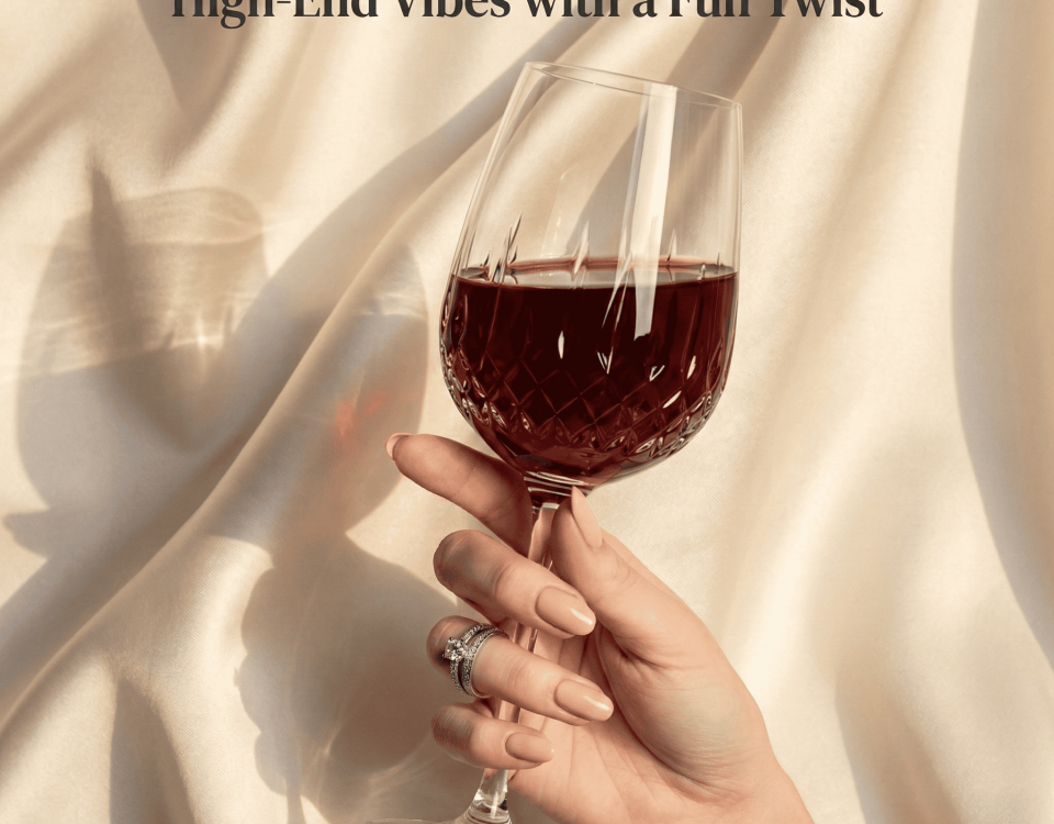 A hand holds a wine glass with red wine against a silky fabric backdrop.